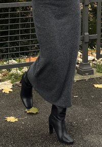 Čierne členkové čižmy na opätku s elegantným dizajnom a hladkou textúrou, v kombinácii s dlhou priliehavou tmavosivou pletenou sukňou.