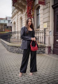 Fekete bőr, oversized blézer egy testhez simuló fekete topon, laza fekete nadrággal párosítva. A megjelenést egy piros kézitáska és átlátszó sarkú szandálok egészítik ki.