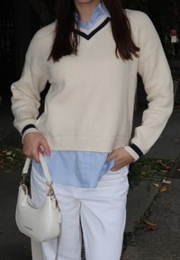 Krémový rebrovaný sveter s námorníckym lemom, vrstvený cez svetlomodrú košeľu s golierom. Kombinovaný s bielymi nohavicami a malou bielou kabelkou.