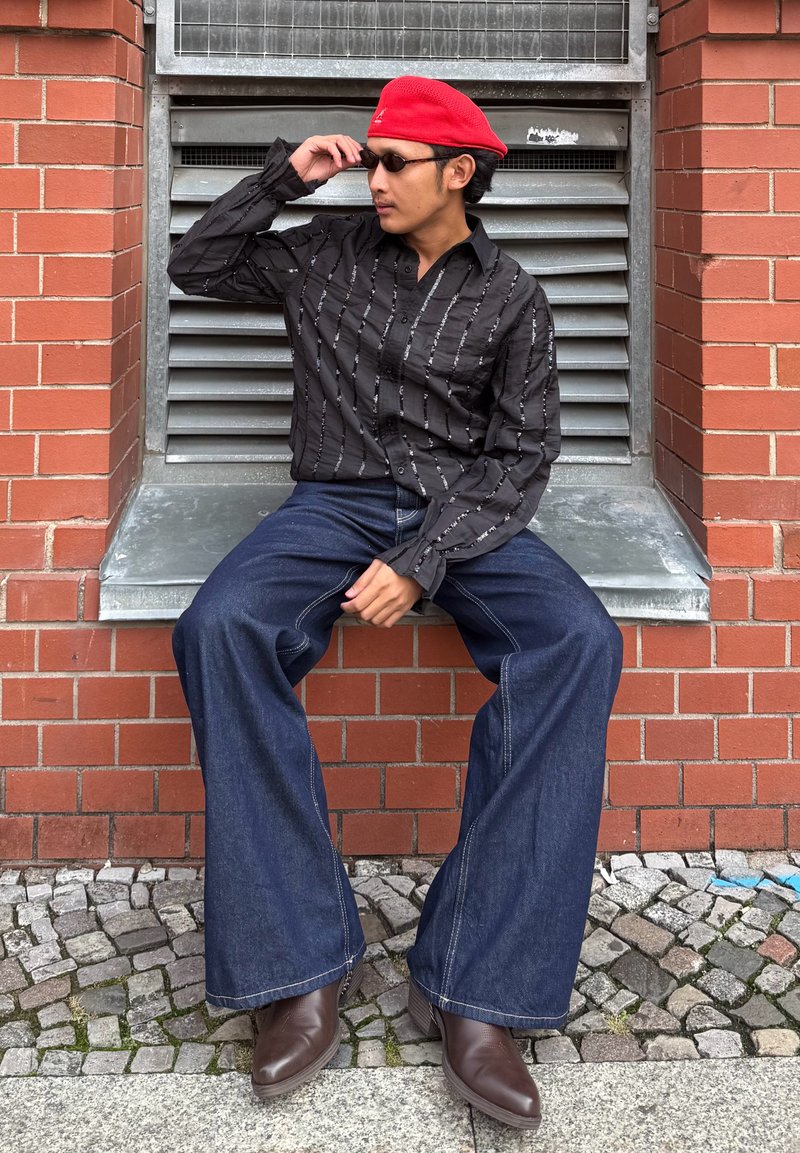 Black button-up shirt with white vertical stripes, flared dark blue jeans, and brown leather boots. Red beret and sunglasses as accessories.