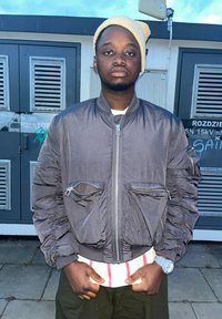 Šedá vypolstrovaná bomber bunda so zipsovým zapínaním, má dve predné vrecká so zipsami, nosená cez bielo-červené pruhované tričko.