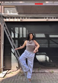 Pantalones de chándal grises, top de canalé beige y un bolso rosa claro. De pie en una escalera de metal contra un fondo negro con sombras.