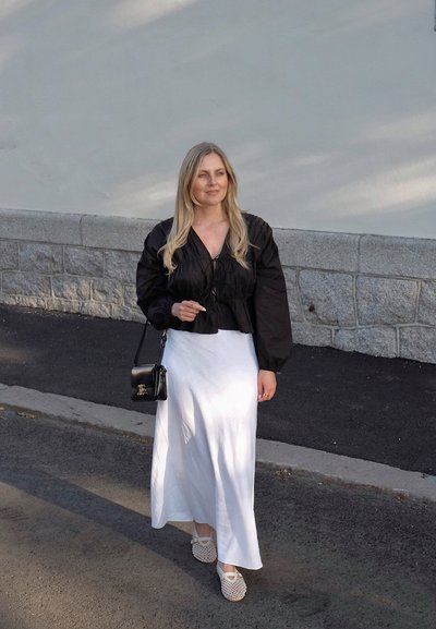 Cazadora negra texturizada y corta con mangas abullonadas, combinada con una larga falda blanca. El accesorio incluye un pequeño bolso negro y zapatos de esparto.