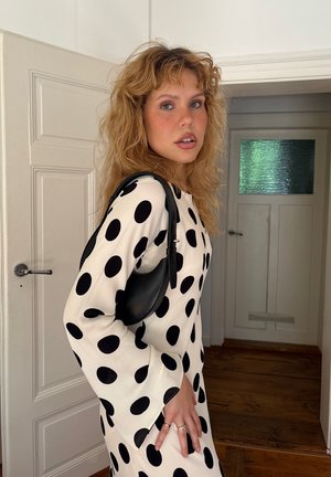 Vestido negro y blanco con lunares, de manga larga y tejido texturizado, combinado con un pequeño bolso negro. Suelo de madera natural y puerta de color claro.