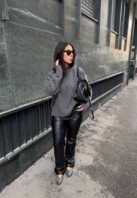 Szürke túlméretezett pulóver, fekete műbőr nadrág, fekete táska szegecsekkel, és ezüst részletekkel díszített hegyes orrú cipők egy városi utcán.