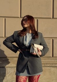 Szary żakiet w prążki z zapięciem na pasek, połączony z jasnoszarym swetrem, dżinsową spódnicą i czerwonymi koronkowymi rajstopami. Trzymany biały torebka.