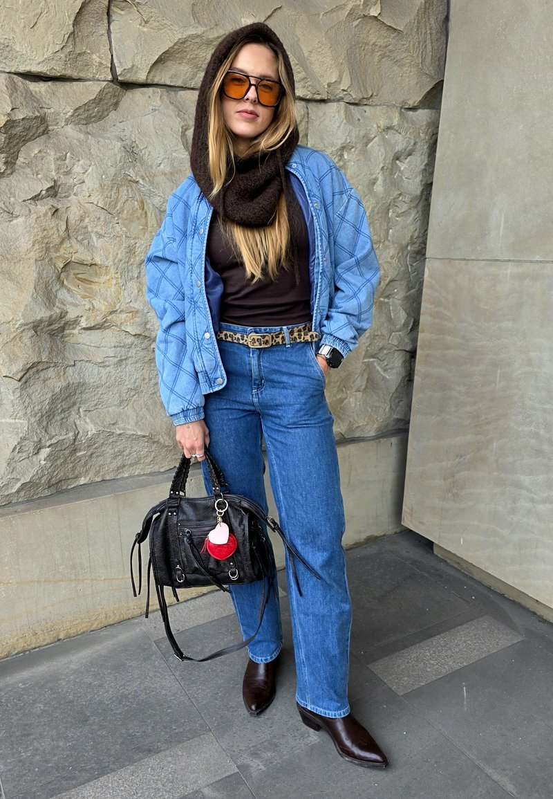 Denim jacket with quilted pattern, brown knitted scarf, black handbag with pink and red accents, blue jeans, and brown pointed boots.