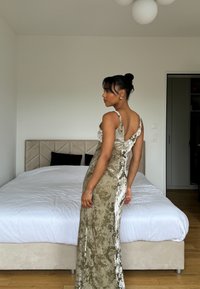 Robe vert olive avec une silhouette ajustée et des accents en dentelle ; elle présente de fines bretelles et un dos en V profond. Texture lisse, design longueur de sol.