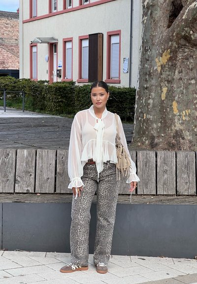 Blusa blanca y transparente con puños acampanados, combinada con pantalones de estampado de leopardo. Accesorios con un bolso ligero y zapatillas casuales marrones.