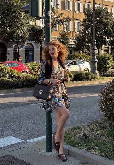 Vestido fluidos con estampados florales y de animales, con un escote en V profundo y dobladillo con volantes. Bolso marrón con acentos metálicos y mocasines marrones.