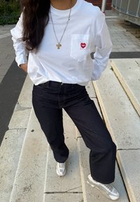 Valge pika varrukaga shirt punase südame tasku disainiga, koos tumesiniste laia säärega teksade ja valgete ketsidega, millel on silmaaugud.