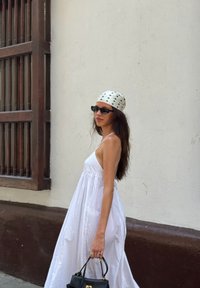 Maxi white dress with a relaxed fit, thin straps, and gathered waist. Black handbag and polka-dot white headscarf. Set against a neutral backdrop.