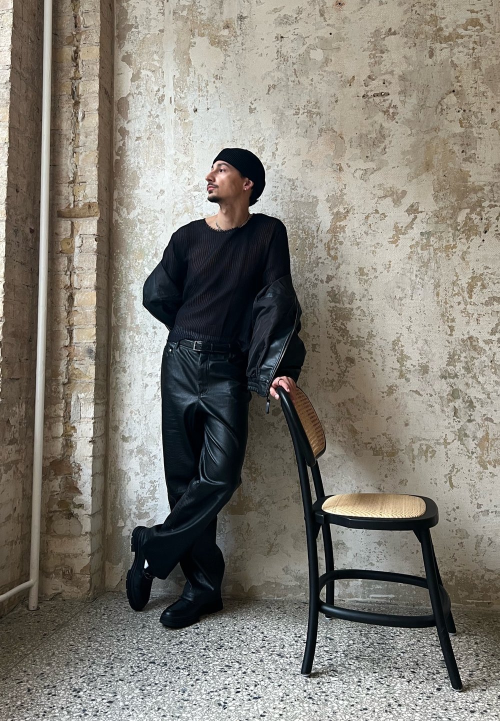 Melnas ribotas garās piedurknes augšdaļa ar pārspīlētām melnām piedurknēm, apvienota ar spīdīgām melnām ādas biksēm. Izskatu papildina melns beanie cepure un masīvas melnas kurpes.