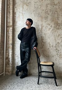 Melnas ribotas garās piedurknes augšdaļa ar pārspīlētām melnām piedurknēm, apvienota ar spīdīgām melnām ādas biksēm. Izskatu papildina melns beanie cepure un masīvas melnas kurpes.