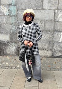 Black and white checkered tunic featuring a white Peter Pan collar, teamed with grey wide-leg jeans and a black handbag adorned with decorative charms.