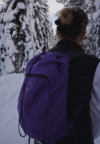 Purple backpack crafted from durable fabric with a sleek design, featuring adjustable straps, a top handle, and a prominent logo.