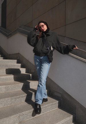 Chaqueta negra de gran tamaño, jeans de campana de color azul claro y zapatos gruesos negros. Los accesorios incluyen un bolso bandolera negro y una diadema.