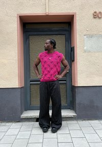 Κίτρινο αμάνικο τοπ σε φωτεινό ροζ με ανοιχτό σχέδιο, συνδυασμένο με φαρδιά παντελόνια μαύρες ρίγες και χοντρά μαύρα υποδήματα.