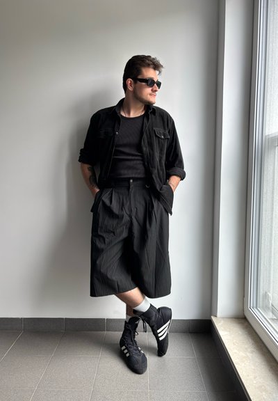 Camisa negra de manga corta sobre una camiseta sin mangas negra de canalé, combinada con pantalones cortos negros con rayas. Zapatillas altas negras con franjas blancas.