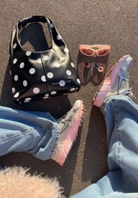 Sac à main à pois, lunettes de soleil roses forme œil de chat, trois bagues, et personne portant des baskets roses et grises avec un jean bleu clair sur l'asphalte.