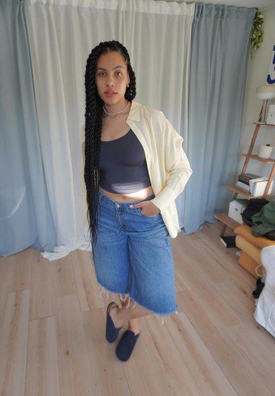Camisa de botones a rayas amarilla clara sobre un top negro corto, combinada con culottes de mezclilla azules y zapatos náuticos azul marino.