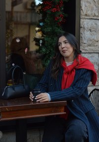 Sac à main noir avec des poignées arrondies à côté d'une personne tenant une tasse de café. La personne porte un manteau bleu marine à fines rayures avec une écharpe rouge.