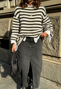 Μαύρο και άσπρο ριγέ πουλόβερ από πλέγμα με φαρδιά μανίκια, συνδυασμένο με μαύρη τζιν φούστα με εμπρός σχισμή και μαύρες μπότες.