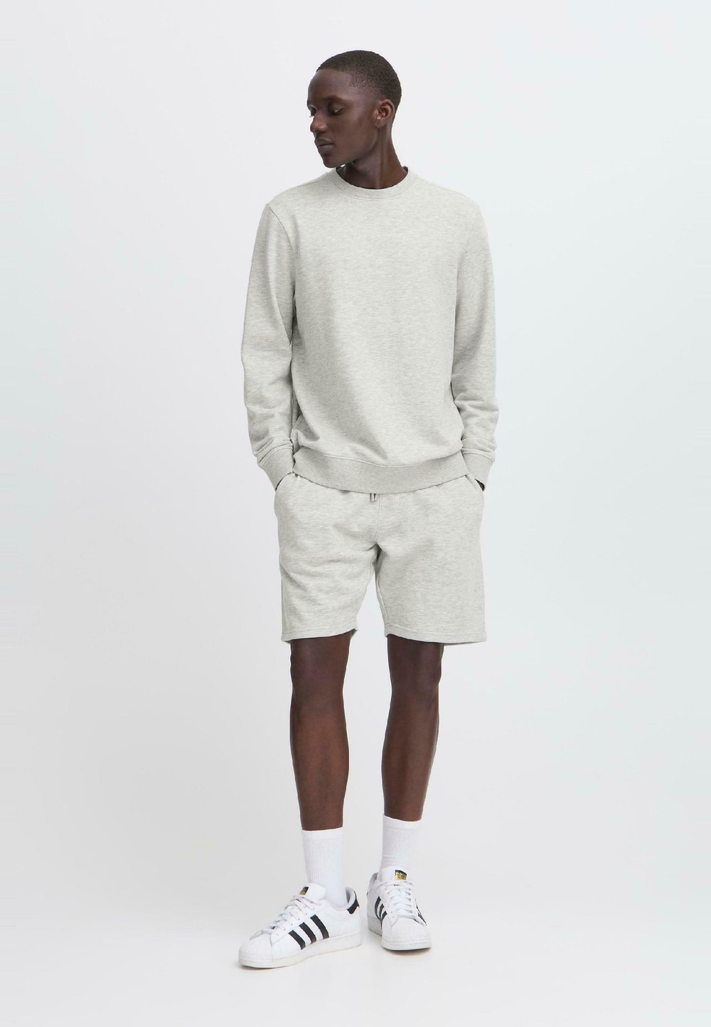 Felpa grigia e pantaloni corti abbinati in tessuto morbido, con polsini elasticizzati. Indossati con scarpe da ginnastica bianche e calze. Taglio semplice e casual.