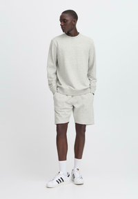 Felpa grigia e pantaloni corti abbinati in tessuto morbido, con polsini elasticizzati. Indossati con scarpe da ginnastica bianche e calze. Taglio semplice e casual.