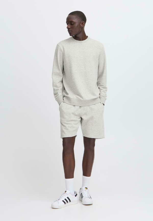 Szürke pulóver és hozzáillő rövidnadrág puha anyagból, rugalmas mandzsettákkal. Fehér sportcipővel és zoknival viselve. Egyszerű, laza szabás.