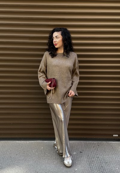 Suéter beige de gran tamaño con mangas acampanadas, combinado con pantalones de pierna ancha plateados y brillantes. Sosteniendo un clutch burdeos con una cadena.