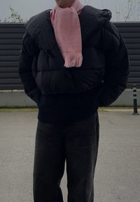 Doudoune noire avec capuche, associée à une écharpe rose clair à franges. Un pantalon sombre et ample complète la tenue.