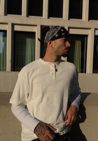 Bijela rebrasta majica kratkih rukava složena preko tijesne majice dugih rukava, crna bandana i crne hlače s metalnim detaljima.