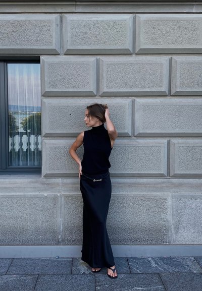 Top negro sin mangas con un cuello alto, combinado con una falda larga negra que presenta un acento de cinturón metálico. Tejido suave, diseño minimalista.