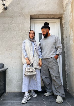 Chaleco acolchado gris claro sobre un vestido largo gris. Sudadera gris y pantalones cargo. Zapatillas plateadas y un pequeño bolso blanco con detalles.