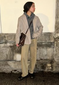Ανοιχτό γκρι μάλλινο σακάκι πάνω από ένα σκούρο γκρι πουλόβερ, συνδυασμένο με μπεζ παντελόνι και μαύρε�ς γόβες μέχρι τον αστράγαλο, κρατώντας μια καφέ τσάντα ώμου.