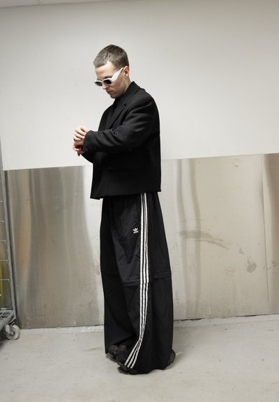 Blazer negro de gran tamaño sobre un cuello de cisne negro, combinado con pantalones deportivos anchos con tres franjas blancas. Incluye gafas de sol blancas.