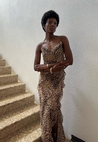 Vestido de estampado de leopardo com bainha ondulada, alças finas e acabamento em cetim. Usado por uma pessoa em pé perto de degraus de pedra.