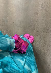 Brilliant pink handbag with a structured design, being held with a turquoise outfit featuring a floral pattern, complemented by bright pink clogs on a grey surface.
