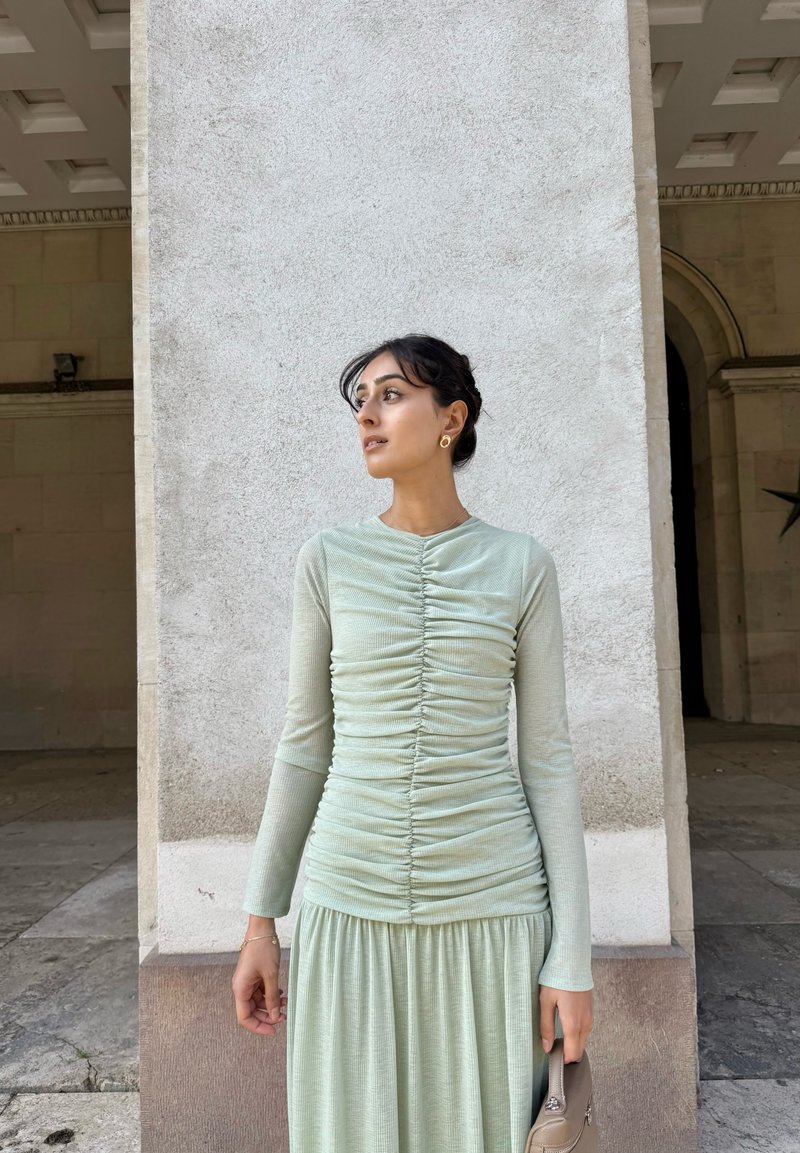 Top a maniche lunghe di colore verde chiaro con texture arricciata, abbinato a una gonna coordinata. Tessuto morbido, design minimalista e lucentezza sottile.