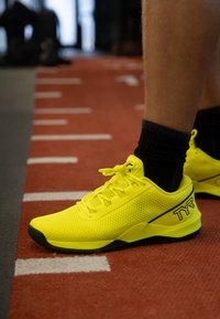 Scarpe sportive gialle con tomaia in mesh, design con lacci e dettagli neri; suola in gomma e particolari testurizzati per una migliore aderenza.