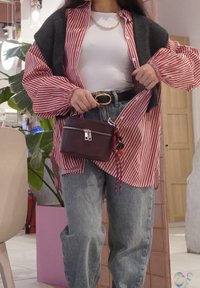 Piros-fehér csíkos, oversized ing, fehér felsővel rétegezve, világoskék farmerral és kis bordó oldaltáskával párosítva. Arany lánc nyaklánc.