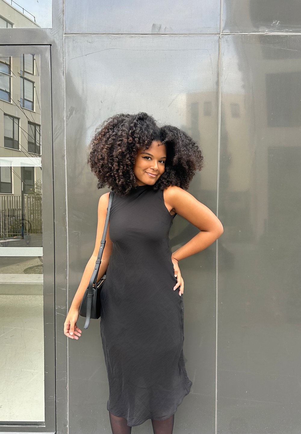 Svart ärmlös klänning med en subtil texturerad mönster, figurnära siluett och kjol i medellängd. Kombineras med en liten svart axelväska.