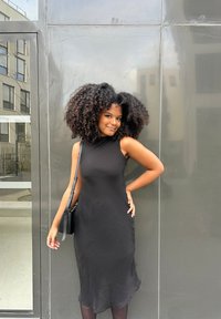 Svart ärmlös klänning med en subtil texturerad mönster, figurnära siluett och kjol i medellängd. Kombineras med en liten svart axelväska.