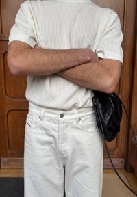 Witte geribbelde trui met korte mouwen, witte spijkerbroek en een zwarte leren crossbodytas. Details omvatten zilverkleurige hardware en gestructureerde stof.