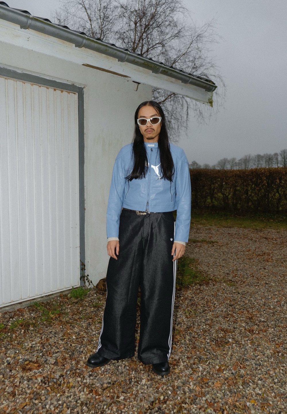 Veste courte bleu clair avec fermetures éclair, pantalon large noir avec des rayures blanches, et bottes noires. Accessoires comprenant des lunettes de soleil blanches.