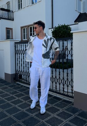 Camisa de manga corta con estampado abstracto negro sobre fondo blanco, combinada con pantalones de lino blancos sueltos y zapatillas blancas.
