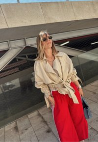 Bežna lanena jakna z dolgimi rokavi, kombinirana s rdečimi širokimi hlačami s belimi črtami. Dodatki vključujejo črne sončna očala in modro torbico.