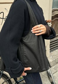 Čierna kožená taška s minimalistickým dizajnom a mäkkou, hladkou textúrou. Má široké popruhy a jednoduchý, nezdobený štýl.