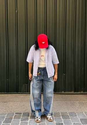 Gorra roja con logo, camisa de manga corta a rayas, camiseta blanca, vaqueros holgados azules con rayas laterales, y zapatos de estampado de vaca.